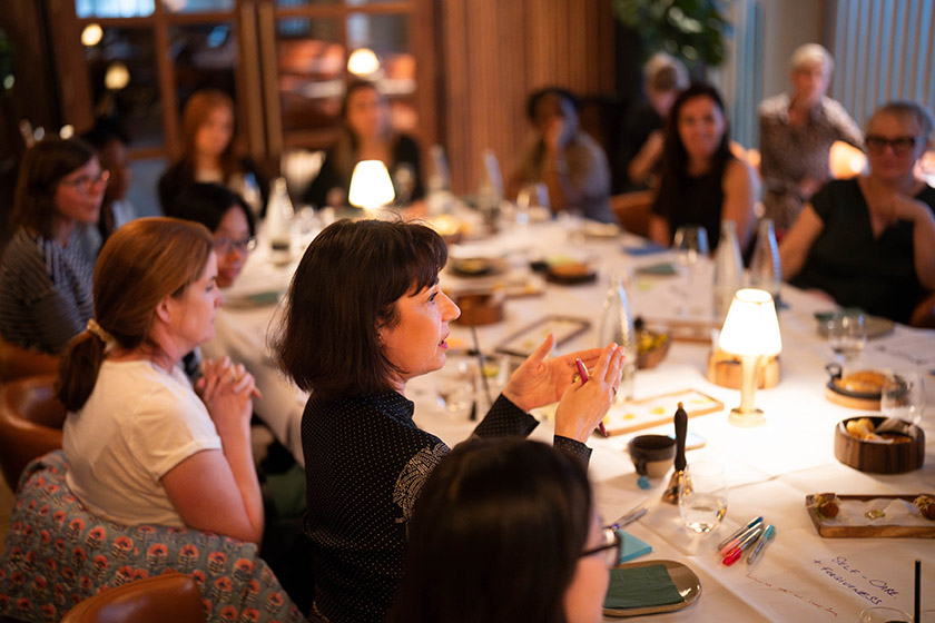 Group of people engaged in conversation at a dining table in a well-lit restaurant setting.